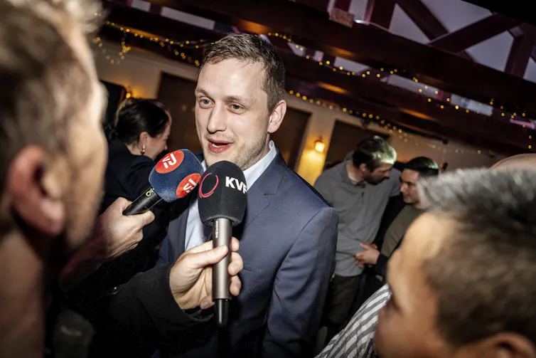 A man in a suit speaking into microphones held by journalists.