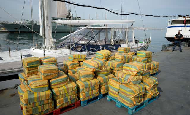 Dezenas de fardos com cocaína empilhados, à frente de um veleiro no porto.