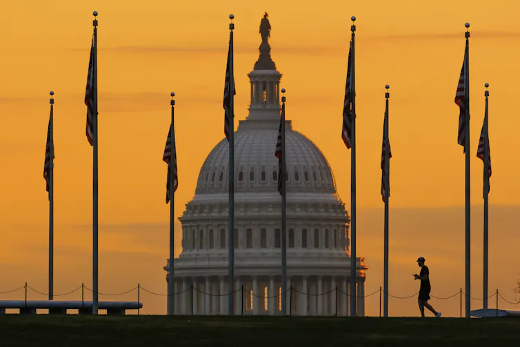 A pedestrian is silhouetted against sunrise with the U.S. Capitol building in the background.