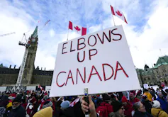 El manifestante tiene codos, una firma canadiense con una torre de mantenimiento de la paz en el fondo.