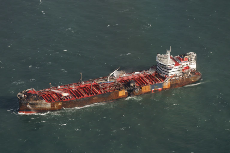 A red oil tanker at sea with a black hole in its hull.