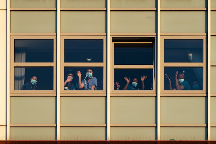 Workers wearing face masks wave from window.