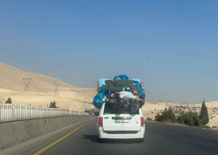 A car with luggage piled on to the roof drives down a road.