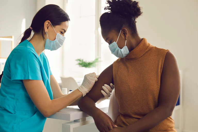 Healthcare worker in a mask gives a vaccine to a woman, also wearing a mask