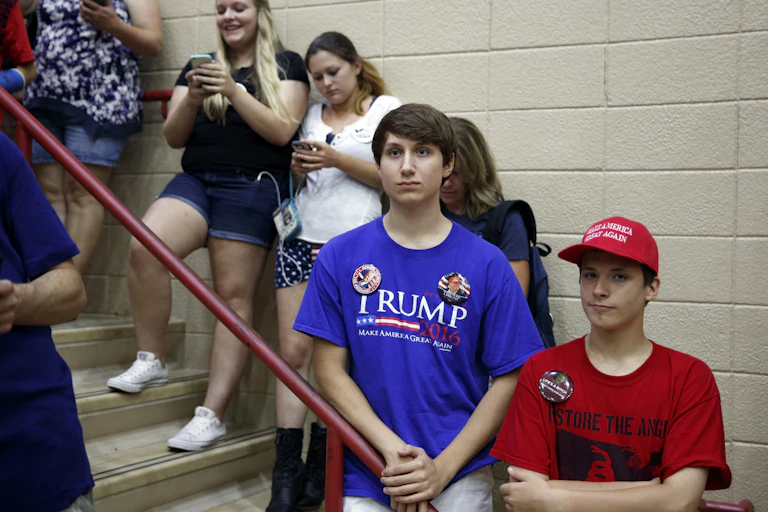Teens standing on a staircase, one in a Trump shirt, another in MAGA hat