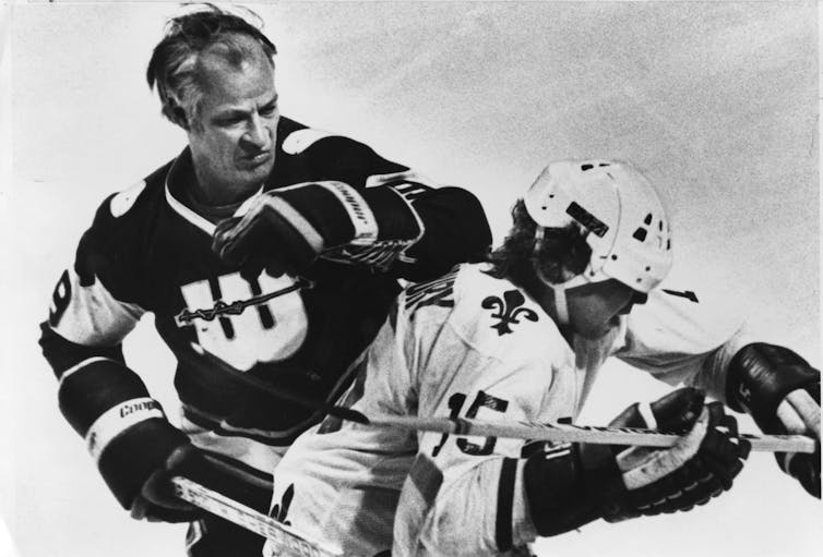 A black and white photo of a hockey player raising his elbow in the direction of another player's head.