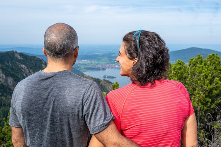 Man in sweaty t-shirt with arm around woman look out at lake.
