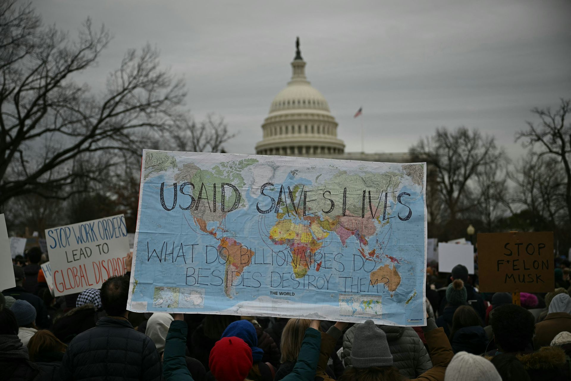 Protester hold up a world map with the words USAID SAVES LIVES on it in front of the US Capitol building.