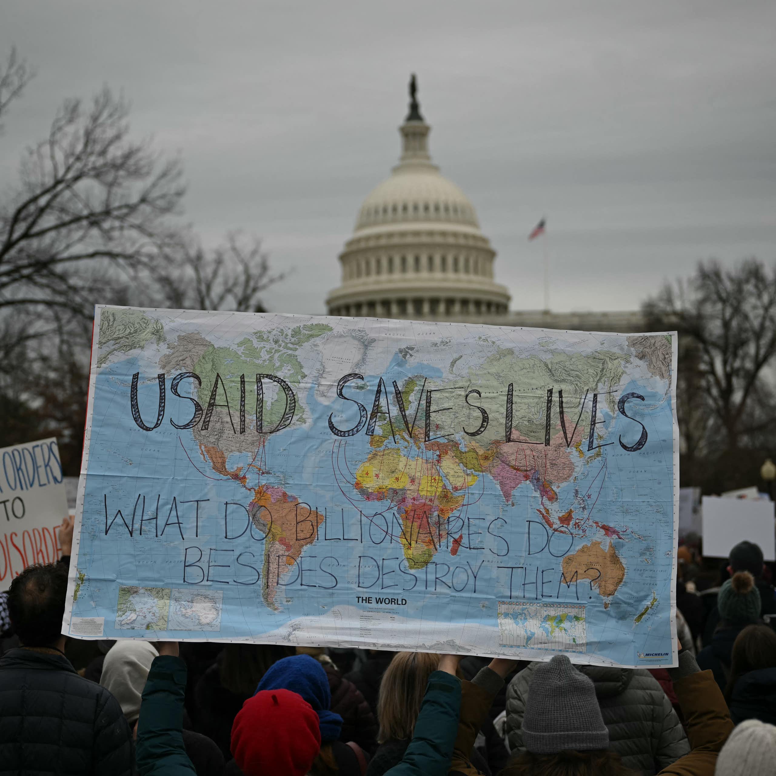 Protester hold up a world map with the words USAID SAVES LIVES on it in front of the US Capitol building.