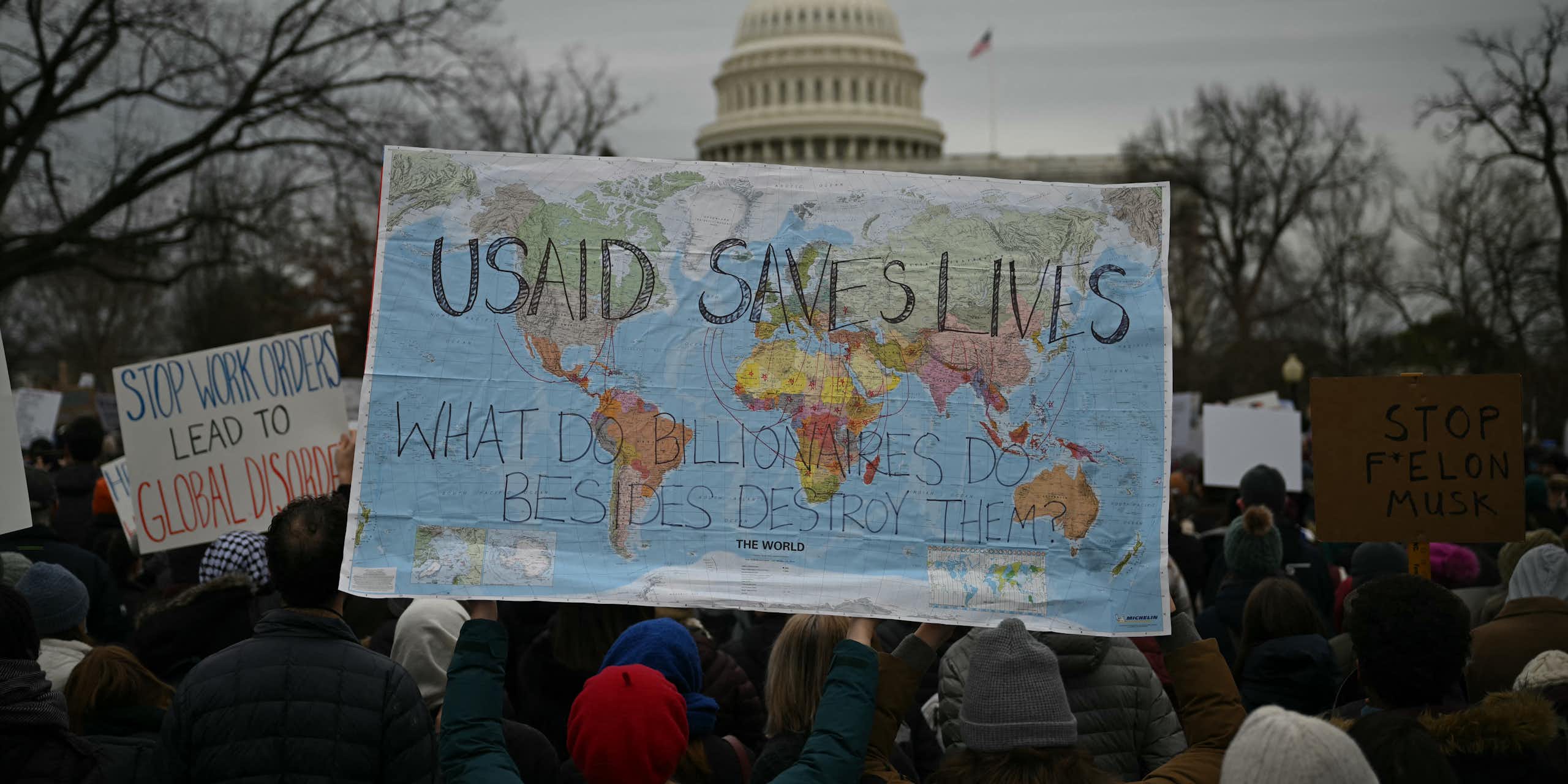 Protester hold up a world map with the words USAID SAVES LIVES on it in front of the US Capitol building.