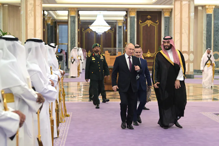 Two men, one in a suit and the other in traditional Gulf attire, walk together.