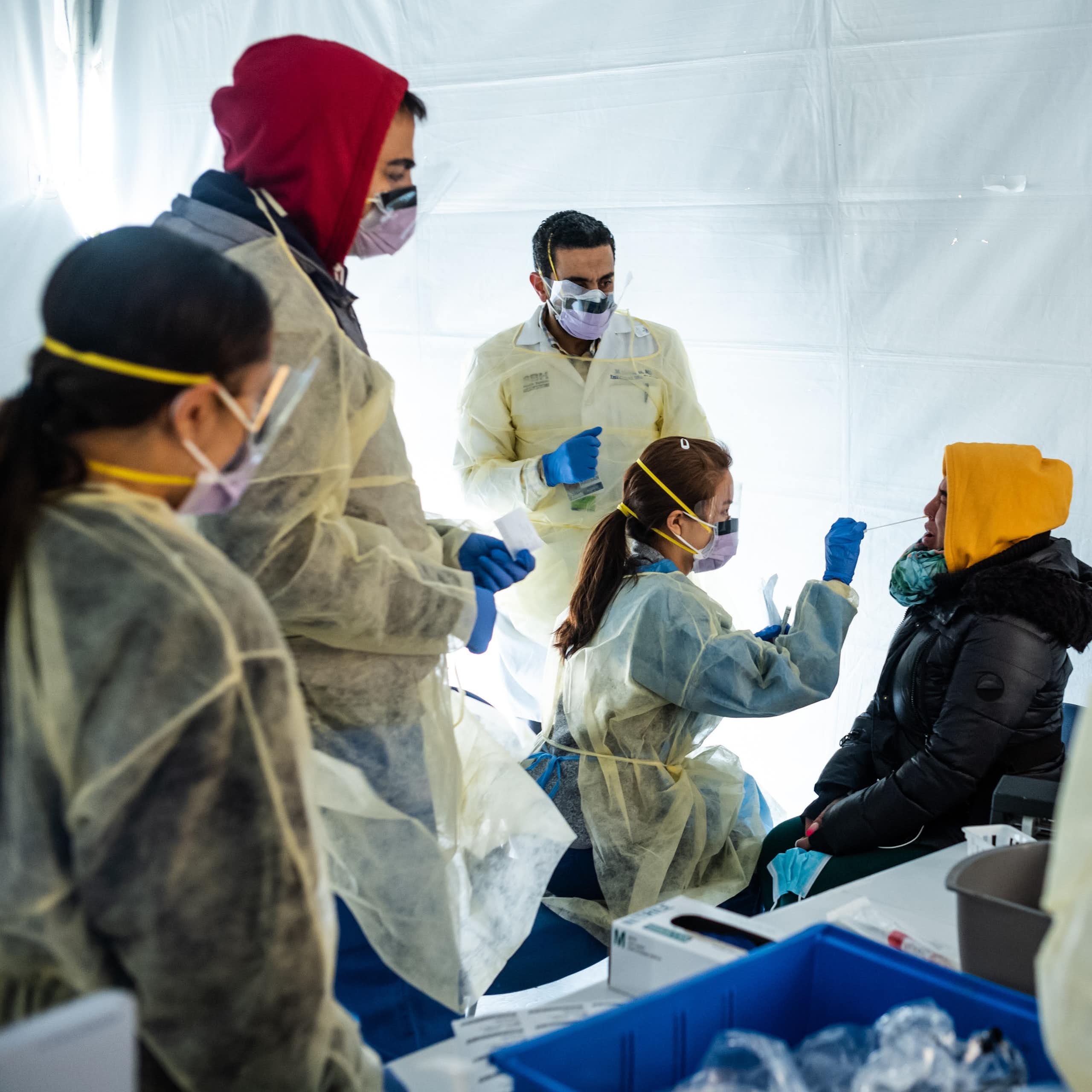 À l'intérieur d'une tente blanche, des médecins portant des masques soumettent un patient à un test de dépistage du COVID-19.