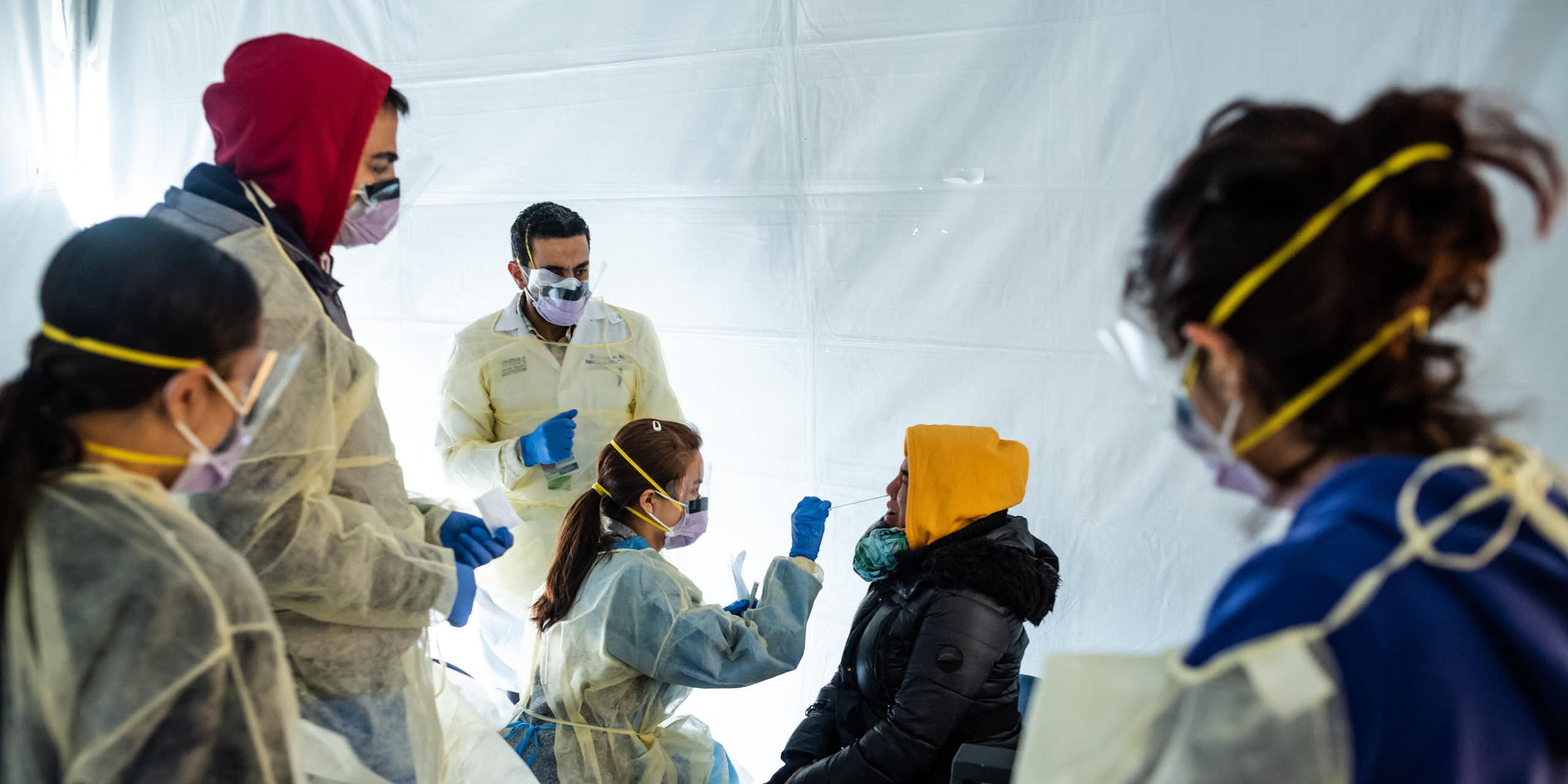 À l'intérieur d'une tente blanche, des médecins portant des masques soumettent un patient à un test de dépistage du COVID-19.