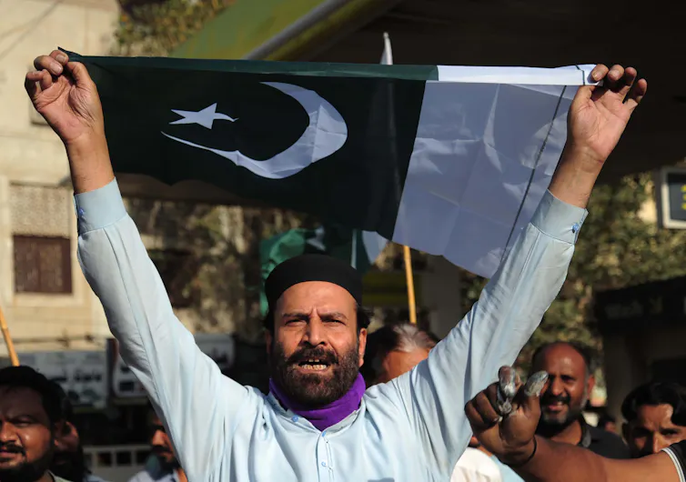 A man at a political rally holding a Pakistan flag.