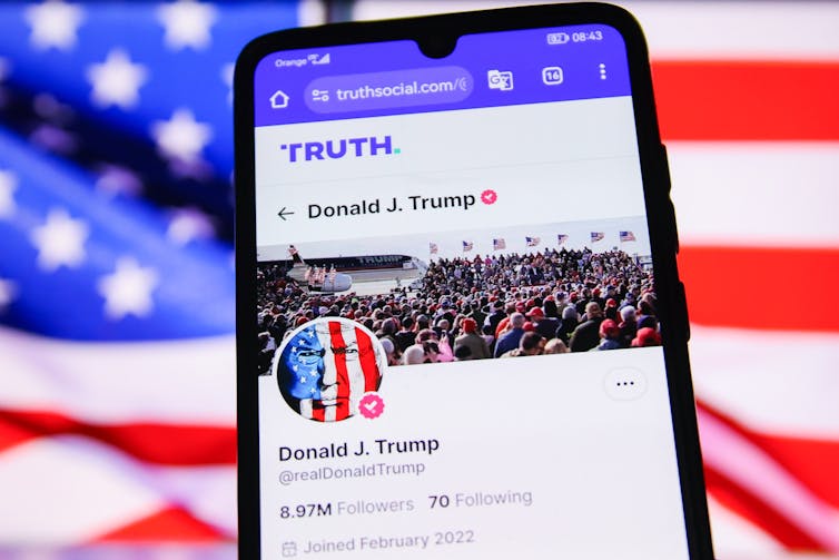 A cellphone showing Donald Trump's social media feed is seen in front of an American flag.