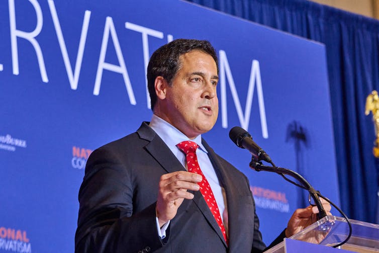 A man in a suit speaks in front of a lecturn.