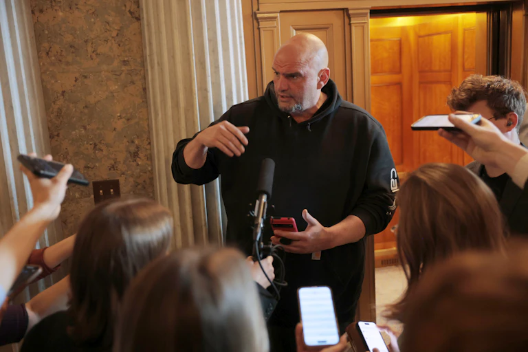 A bald man in a hoodie talking to reporters recording him with cellphones.