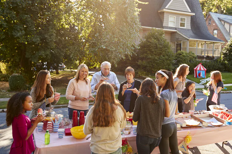 A handful of people of different ages gather around a folding table set on a suburban street.