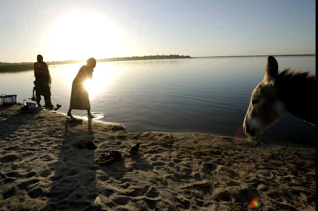 People wash clothes at the edge of Lake Chad with the sunsetting over the water.
