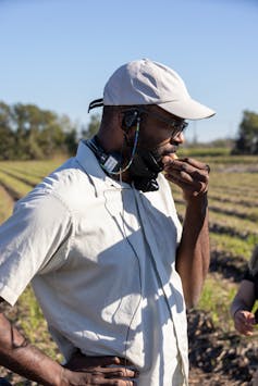 a Black man in a short-sleeved white shirt and white cap, contemplating a field