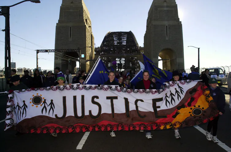 A large crowd of people marching behind a banner than says justice.