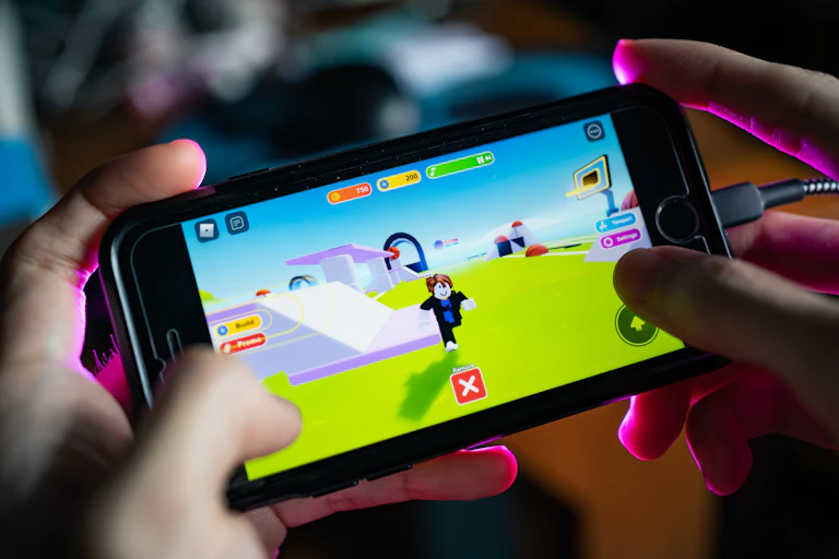 A person's hands as they play a Roblox game on a phone.