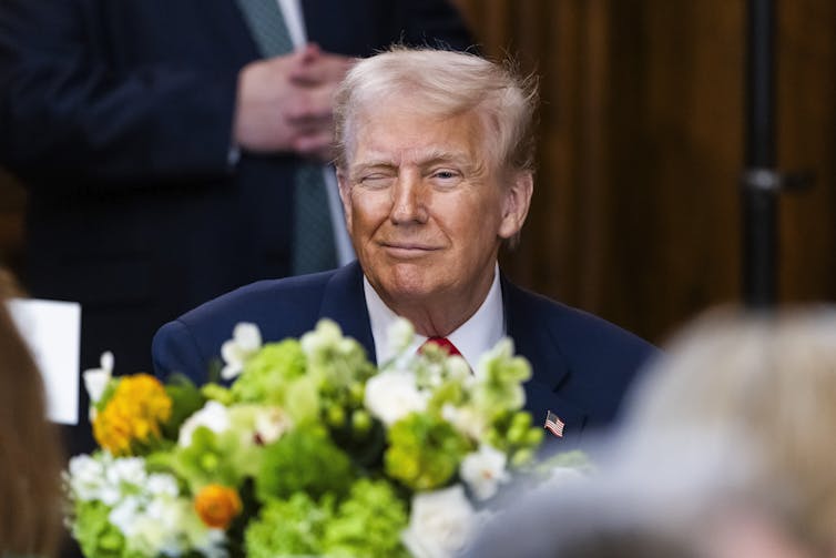Trump winks as he sits at a table.