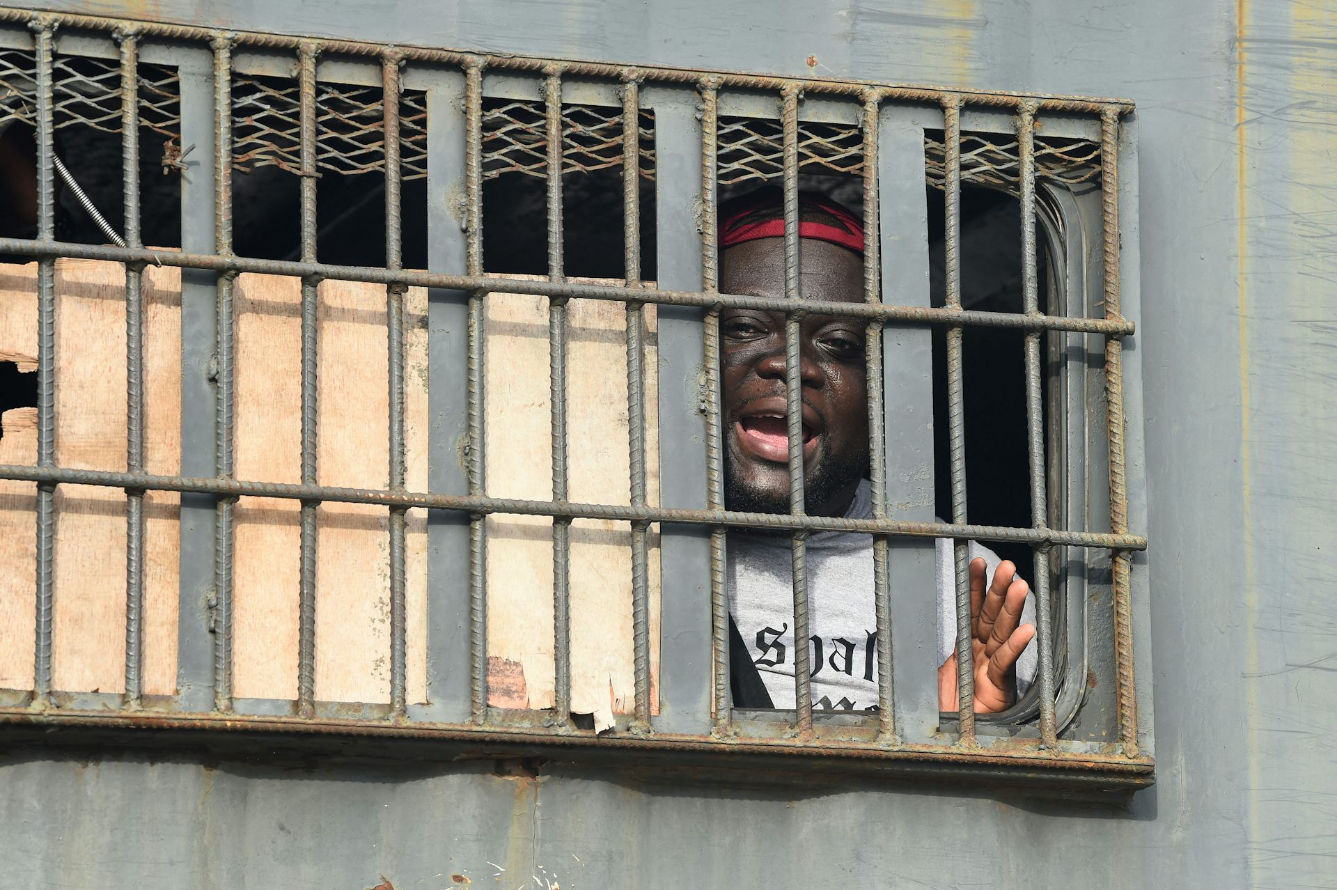 An African man speaks from behind bars in a police van.