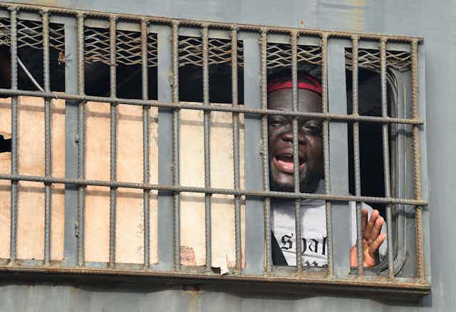 An African man speaks from behind bars in a police van.