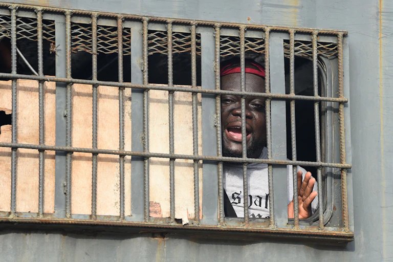 An African man speaks from behind bars in a police van.