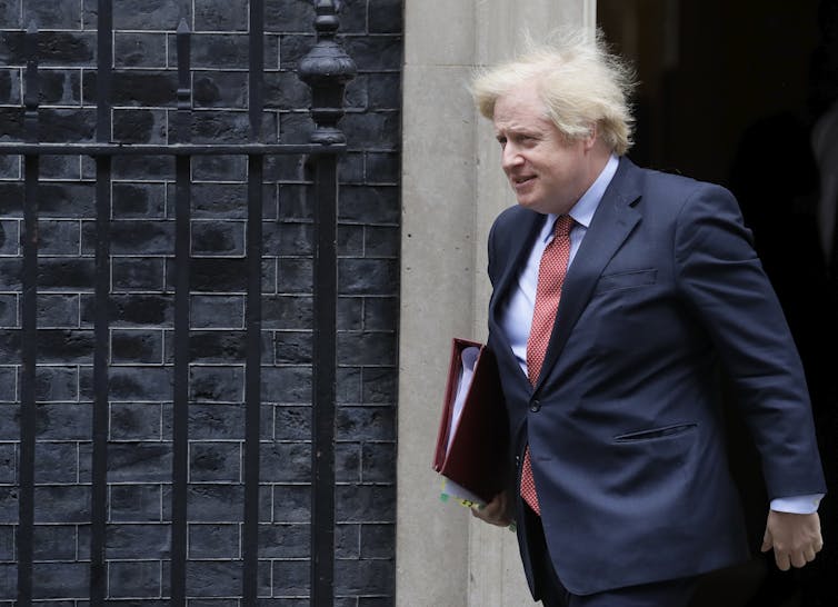 Johson, with blonde hair and a suit, walks out of 10 Downing Street.