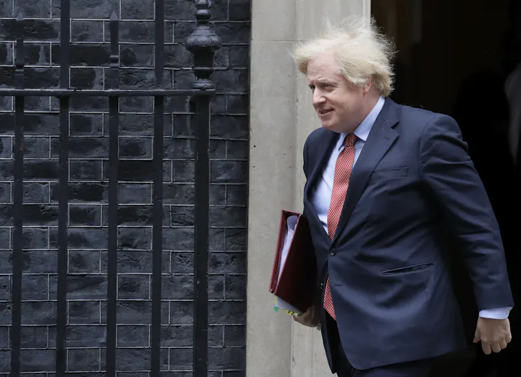 Johson, with blonde hair and a suit, walks out of 10 Downing Street.