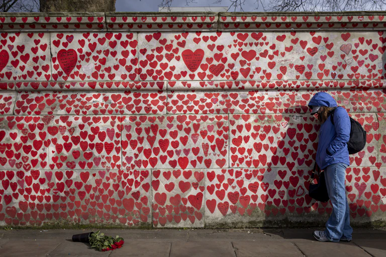 A wall painted with hearts of varying sizes, with a person leaning against it, looking forlorn.