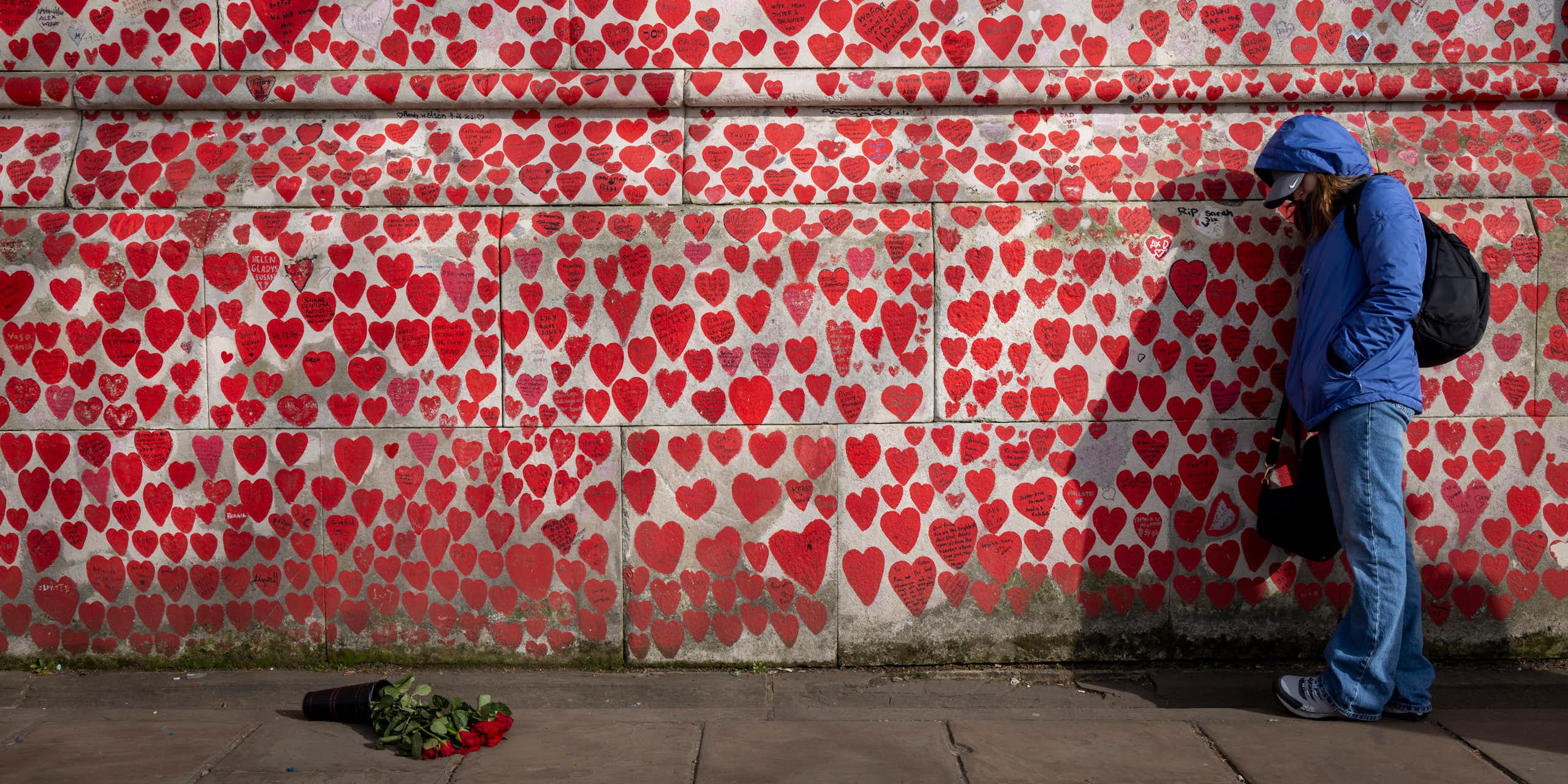A wall painted with hearts of varying sizes, with a person leaning against it, looking forlorn.