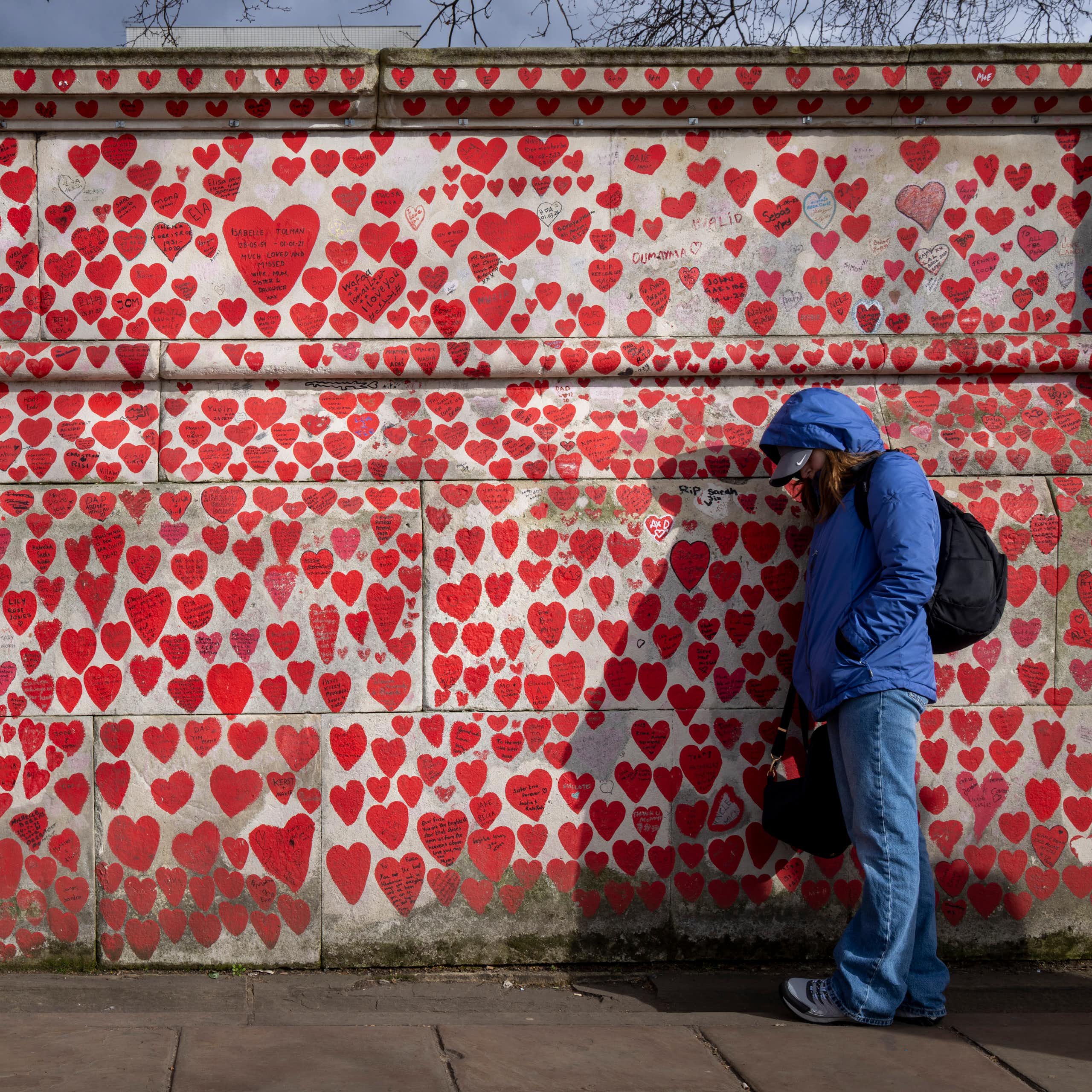 A wall painted with hearts of varying sizes, with a person leaning against it, looking forlorn.