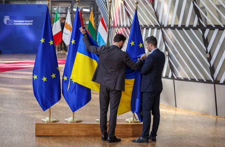 EU officials unfurl a Ukrainian flag next to some EU flags.