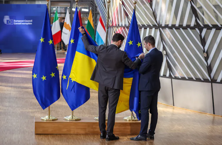 EU officials unfurl a Ukrainian flag next to some EU flags.