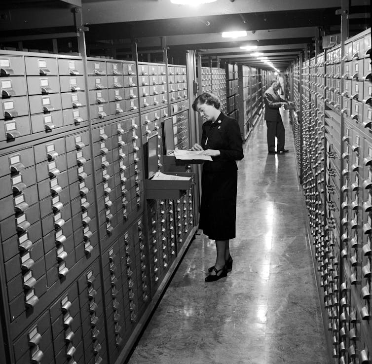 Incendios, guerras y burocracia: varios viajes para establecer un archivo nacional estadounidense 3 Una mujer con un vestido oscuro de pie frente a un enorme gabinete para apilar cajones.