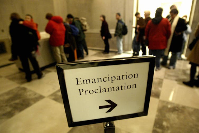 A line stands behind a direction sign that says 'Emancipation Proclamation' on it.