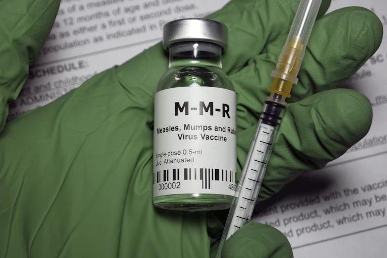 Green glove holding a vial of MMR vaccine and syringe