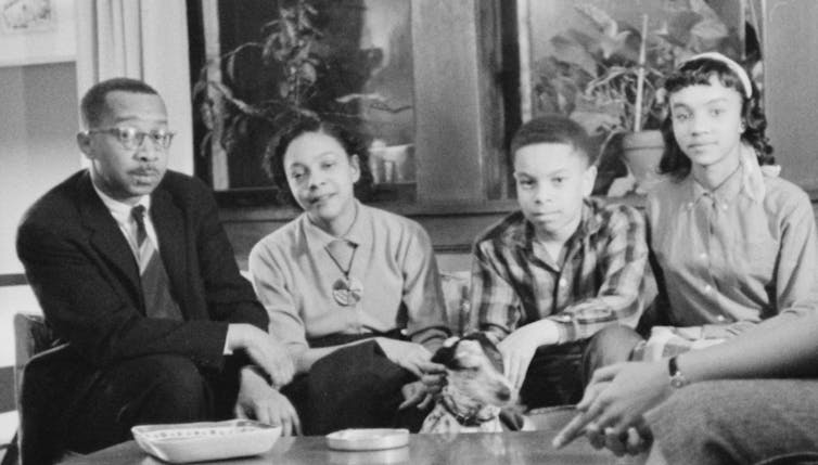 Four people – two adults and two children – sitting on a couch in a vintage photograph.