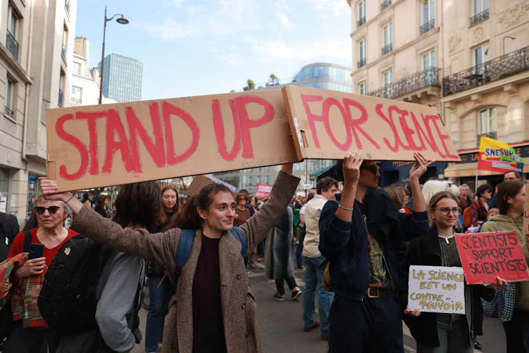 People marching through the street holding a cardboard sign reading "stand up for science"