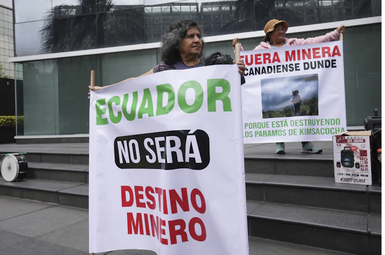 Two Ecuadorian people hold up signs protesting against mining operations in the country. Their signs say: 'Ecuador will not be a mining destiny,' and 'Get out Dunde mining company, because you are destroying Los Paramos of Kimsachocha'