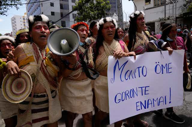 Indigenous people from the Amazon protests in the streets. They carry a sign that says: 'Our territory is not for sale,' which is written in Waorani.