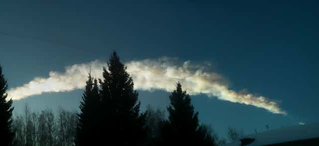 a thick white plume of smoke above a forest