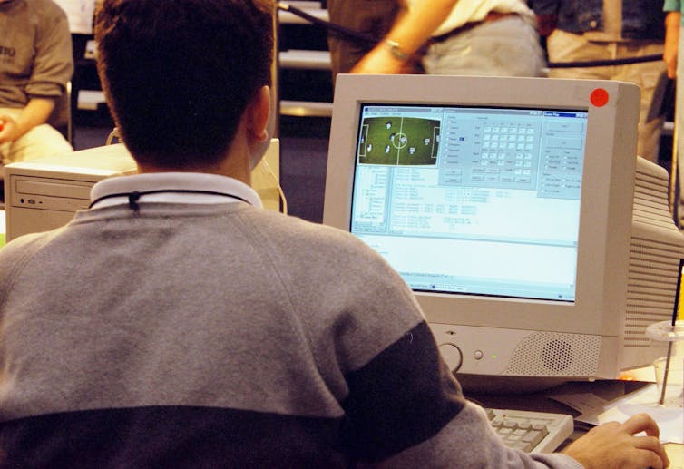 A man sits in front of a large cream desktop computer in the 2000s