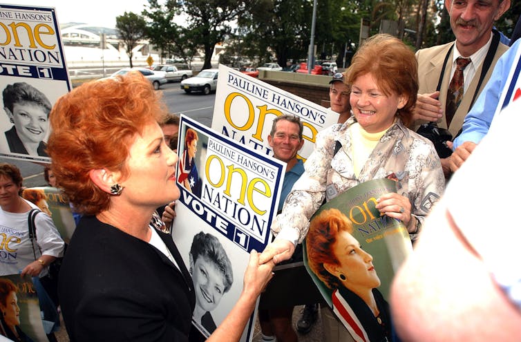 A woman with red hair signs autographs for people holding signs with her face on them