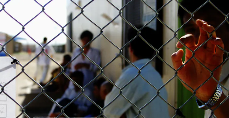 A group of unidentified people gather behind a chicken wire fence