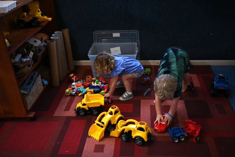 Two young children play with trucks and cars in a daycare centre.