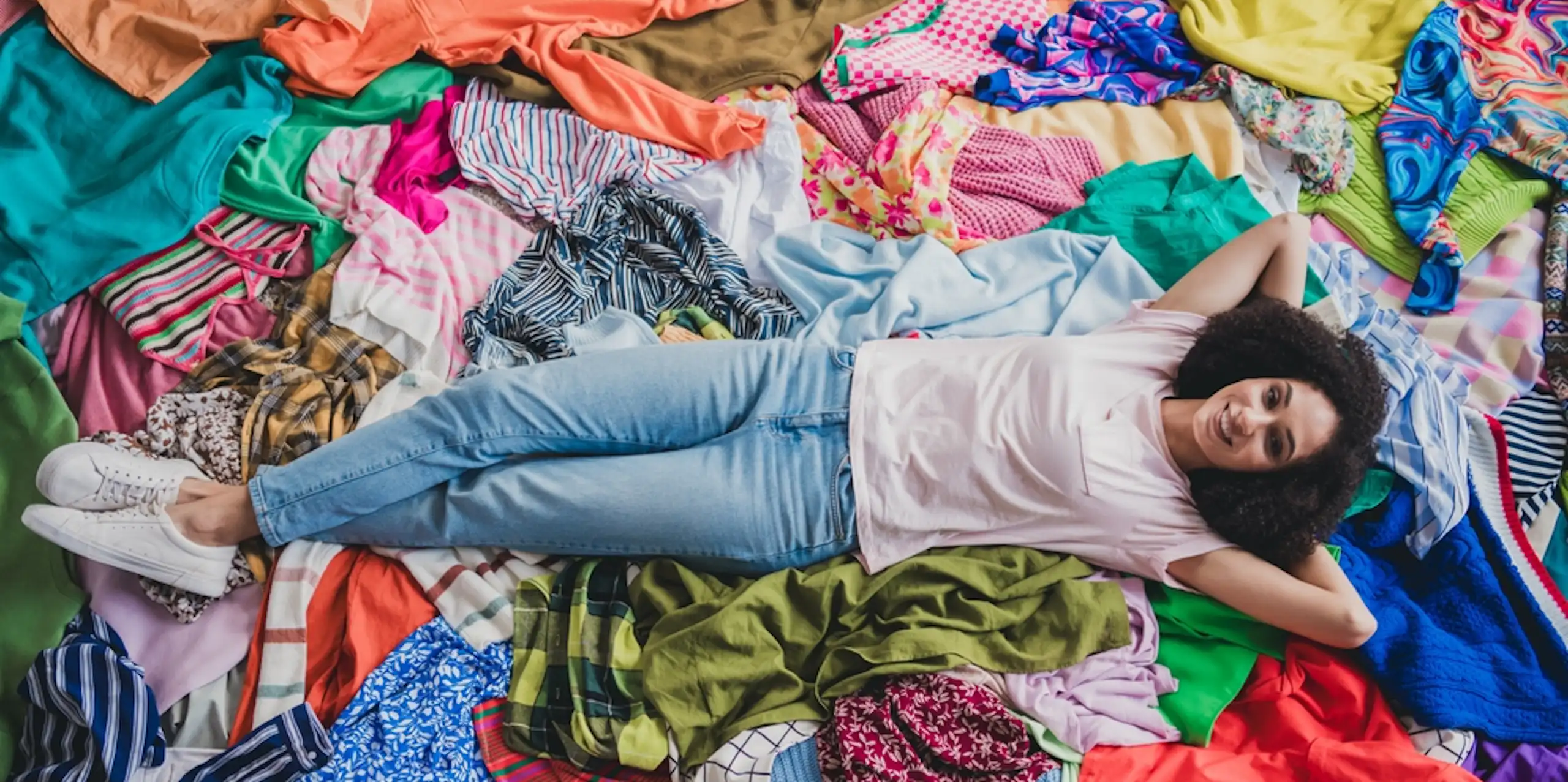 une jeune fille allongée dans sa chambre au milieu de vêtements